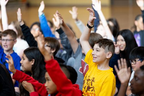 Students raise their hands at an assembly